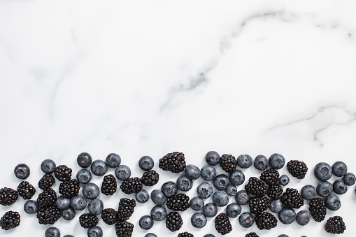 A marble countertop background with fresh blueberries and blackberries with negative space above.