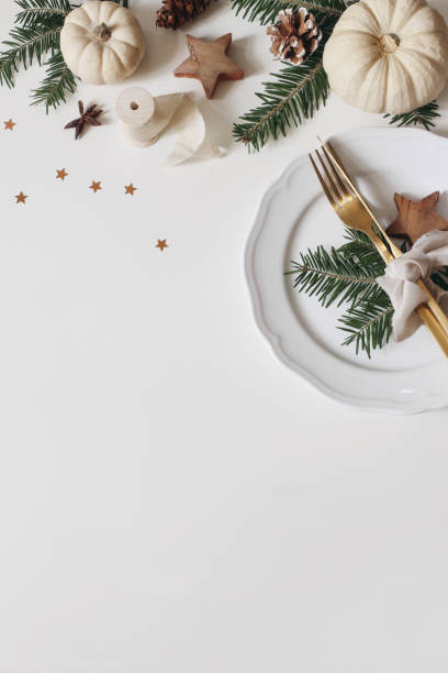 table de noël festive. couverts dorés, branche d’épicéa. citrouilles blanches isolées sur fond blanc. pommes de pin, décoration d’étoiles confettis. composition hivernale. pose plate, vue de dessus, verticale - pine tree pine cone branch isolated photos et images de collection