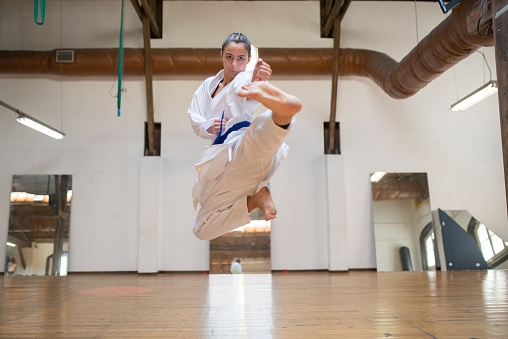 Gorgeous young woman practicing karate. Concentrated woman in white clothes punching air with foot while jumping. Sport, healthy lifestyle concept