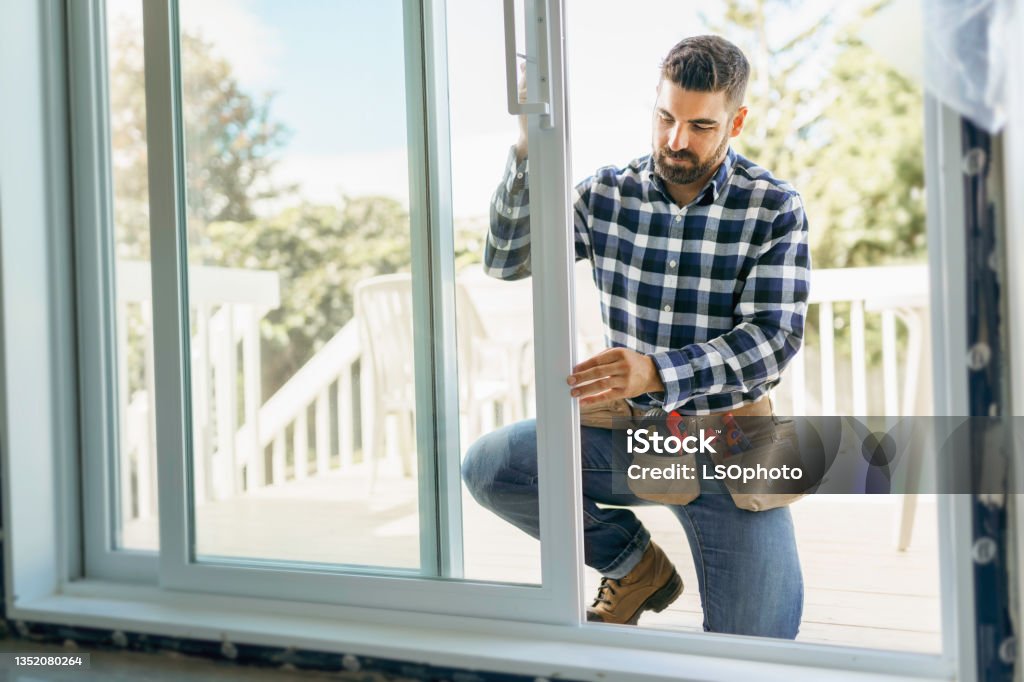 handsome young man installing bay window in a new house construction site A handsome young man installing bay window in a new house construction site Window Stock Photo