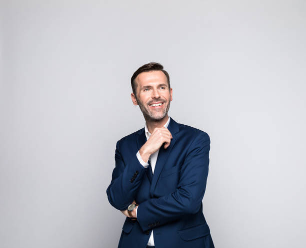 Portrait of happy mature businessman Portrait of mature man wearing suit and white shirt, looking away and smiling. Studio shot of male entrepreneur against grey background. business man looking away stock pictures, royalty-free photos & images