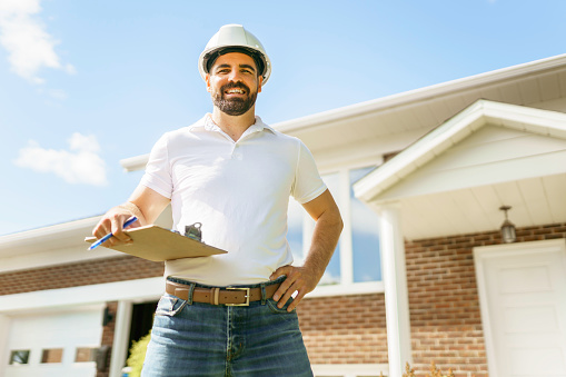 A man with a white hard hat holding a clipboard, inspect house