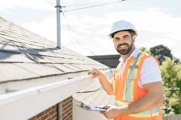 Photo of man in a hard hat, holding a clipboard, standing on the steps of an old rundown house.