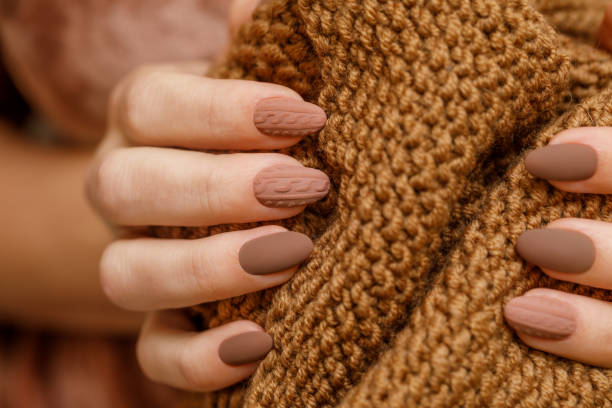 Women's hands with fashionable manicure with a knitted texture on the background of a knitted scarf or plaid. Actual warm shades of autumn in manicure. Matte surface of nail polish Women's hands with fashionable manicure with a knitted texture on the background of a knitted scarf or plaid. Actual warm shades of autumn in manicure. Matte surface of nail polish. Horizontal photo. nude coloured stock pictures, royalty-free photos & images
