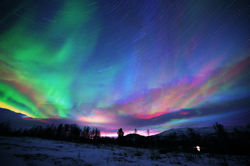 Northern landscape. Winter background with green Aurora Borealis and stars trails