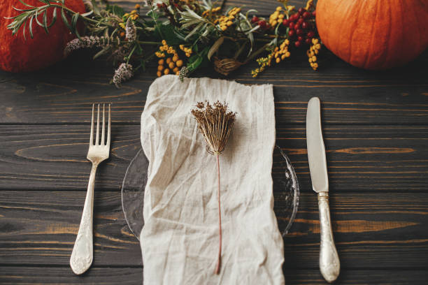 istock Thanksgiving dinner rustic table setting. Modern plate with vintage cutlery, linen napkin, herb on wooden table with pumpkins and autumn flowers arrangement. Eco friendly farmhouse autumn catering 1352085856