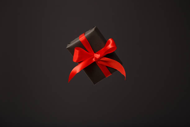 Surprise in flying black gift box with red bow floating in air on black background. Black friday sale, Christmas sale, discount concept. Valentine's day. Father's day