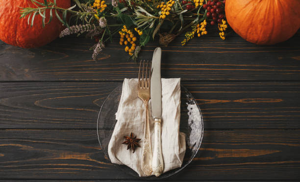 istock Stylish Thanksgiving dinner table setting. Modern plate with vintage cutlery, linen napkin with anise on wooden table with pumpkins and autumn flowers decoration. Farmhouse rustic autumn wedding 1352086782