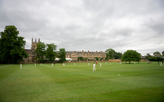 Cricket pitches in front of Merton College.  The college tower is lit by a sunbeam as junior cricketers are on the pitches in front of it. Oxford, Oxfordshire, England, UK.