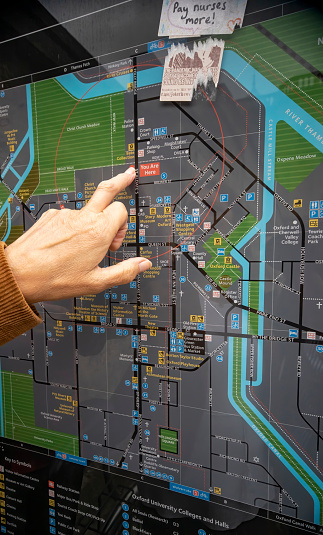 A woman's finger pointing to a 'You are Here' marker of a local public map of Oxford, Oxfordshire, England, UK.
