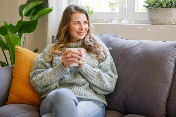 istock attractive middle aged woman sitting on the couch (drinking hot tea) 1352091579