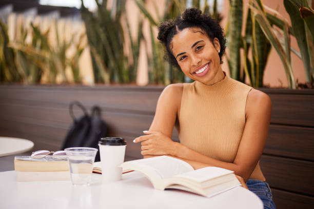istock Cheerful young female university student reading outside at a cafe table 1352091654