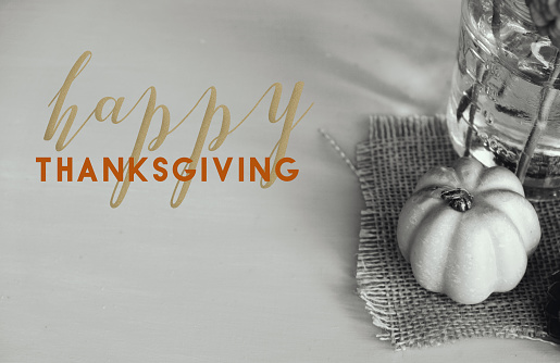 Happy Thanksgiving background with gold and orange text by rustic pumpkin decoration in black and white.
