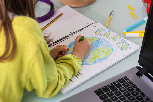 Child girl draws planet earth with wax colors on school notebook for Earth day - Little activist writes the message Save the Planet - Childhood, protection of environment and global warming concept