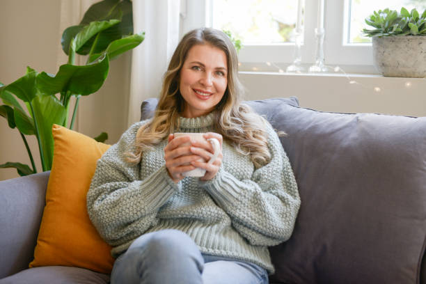 istock attractive middle aged woman sitting on the couch (drinking hot tea) 1352094335