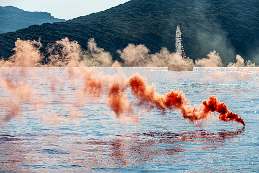 Orange colored smoke grenade in the blue sea. Distress call.