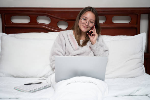 istock Smiling young woman calling in bed 1352095022