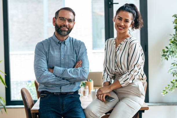 istock Multiage business people taking a break of work while looking at camera sitting on table at modern startup. 1352100321