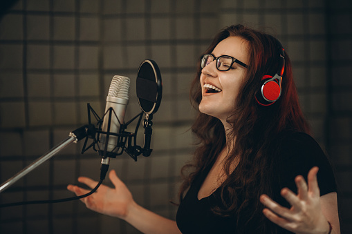 Una persona femenina graba canciones POP en el estudio de grabación. Cantante gesticulando emocionalmente con sus manos. Sala insonorizada para grabación vocal profesional photo