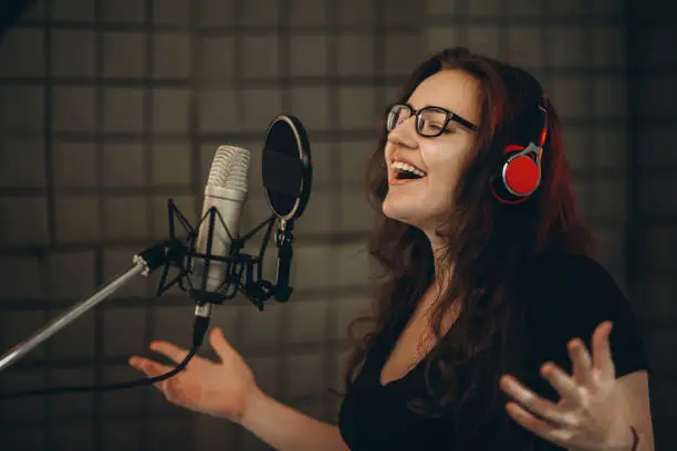 Female person records POP song at the recording studio. Singer emotionally gesturing with her hands. Soundproof room for professional recording vocal