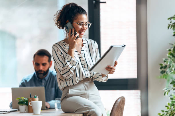 istock Smart businesswoman talking with mobile phone while cheeking some documents in modern workspace. 1352100787