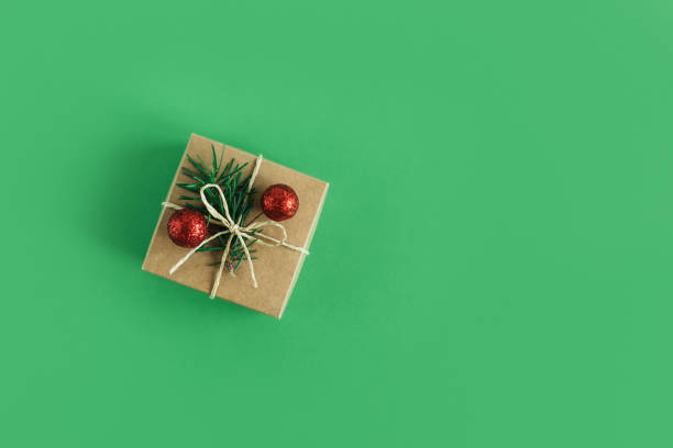 istock Craft gift box with spruce branch and red balls on a green background. 1352102424