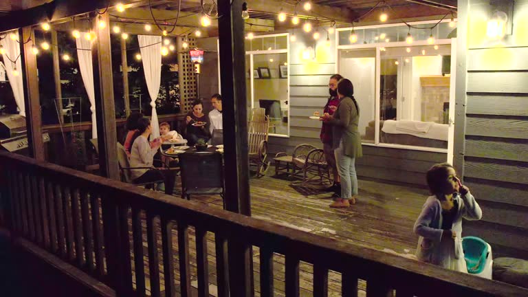 Aerial view of a multi-ethnic group of adults and children enjoying a casual bbq dinner party on a backyard patio on a warm evening.