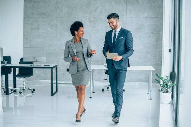 Business conversation in the office. Shot of a two confident business persons talking in the work place. Two colleagues using a digital tablet while walking in a modern office. Businessman and businesswoman in meeting discussing business strategy. Business coworkers working together in the office. african american business couple stock pictures, royalty-free photos & images