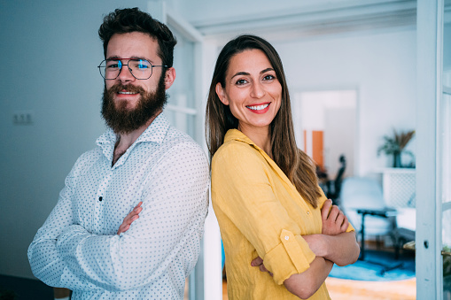 Shot of smiling confident business couple standing back to back and keeping arms crossed while looking at camera.