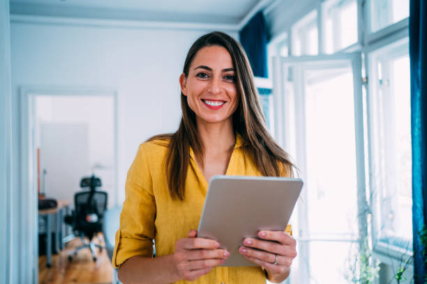 Confident businesswoman in modern office. Shot of beautiful smiling businesswoman standing with digital tablet in hands and looking at camera. sales executive stock pictures, royalty-free photos & images