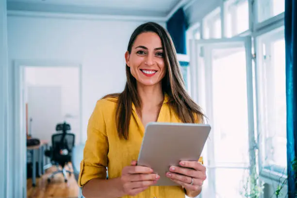 Shot of beautiful smiling businesswoman standing with digital tablet in hands and looking at camera.