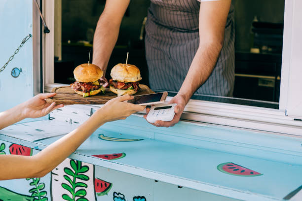 femme achetant des hamburgers dans une camionnette alimentaire et utilisant un smartphone. - food truck photos et images de collection
