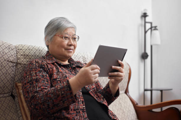 istock An old Asian woman sits on a cloth sofa and uses a tablet computer to chat online 1352105944