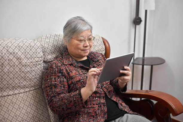 istock An old Asian woman sits on a cloth sofa and uses a tablet computer to chat online 1352106114