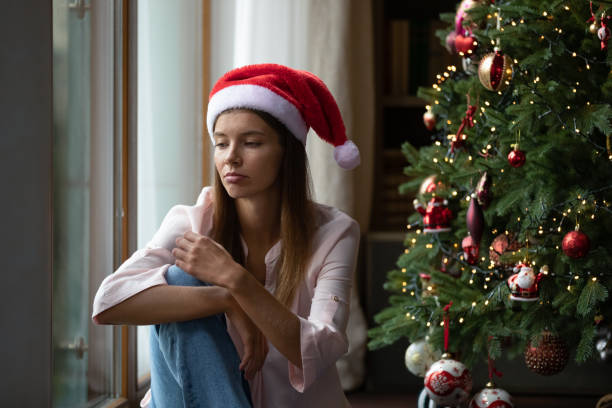 giovane donna di natale frustrata che si annoia all'albero di natale - holiday emotional stress christmas santa claus foto e immagini stock