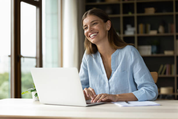istock Happy young employee working at laptop, looking away, smiling 1352107162