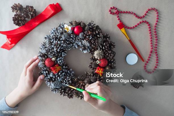 Diy Step 3 Top View Of Florists Hands With Brush Christmas Wreath Of Fir Cones Decorative Toys Stock Photo - Download Image Now