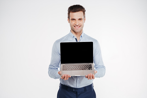 Smiling business man which showing blank laptop screen and looking at camera. Isolated white background