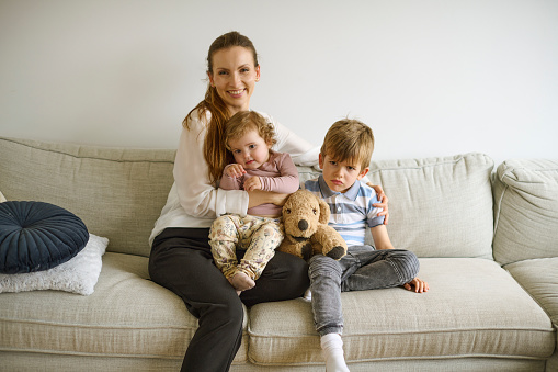 Mother sitting at home in sofa with 2 kids