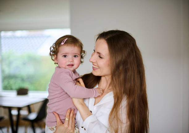 Mother holding her one year old child girl in her arms indoors in the living room