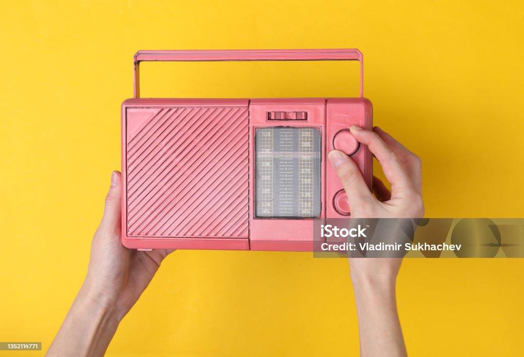 Female hands holding pink fm radio receiver on yellow background. Music minimal concept Stereo Stock Photo