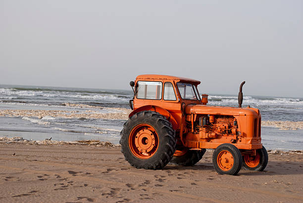 Old tractor with fishing net parked on a sandy beach, ready for work