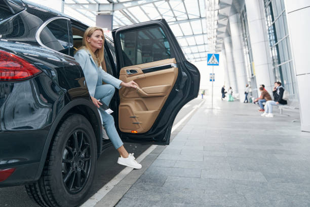 Elegant female passenger getting out of taxi Stylish young Caucasian woman leaving elite car parked before airport terminal building taxi stock pictures, royalty-free photos & images