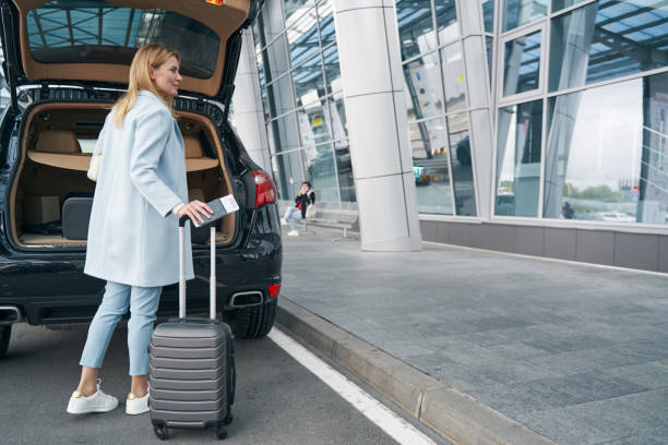 istock Passenger with travel document and baggage near open car trunk 1352121800