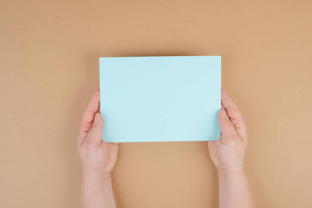 istock Woman holds a blank sheet of paper, brown colored background, empty copy space for text, minimalism 1352122972