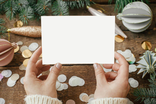 istock Hands holding empty greeting card and christmas ornaments, confetti, pine branches  on rustic wooden background. Christmas card mock up. Space for text. Seasons greetings. Template 1352124474