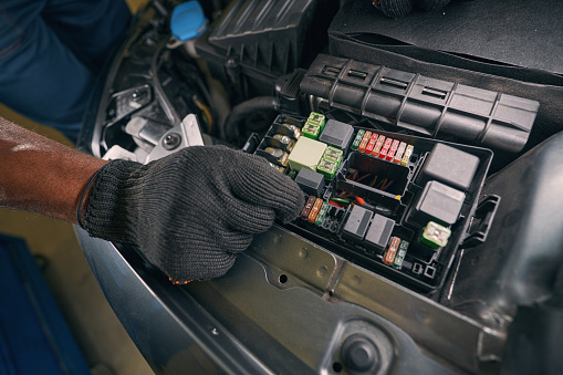 Car service worker replacing automobile fuse in engine