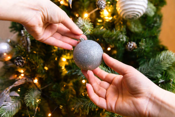 istock Woman hands decorating Christmas tree. Christmas tree with wite and silver decorations, ornaments toy and ball. Modern classical style interior design. Christmas eve at home, time for celebration 1352126710