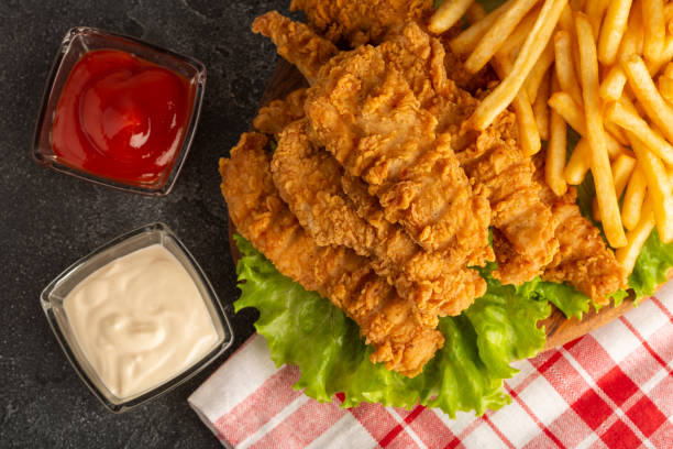 istock Breaded chicken strips with two kinds of sauces and fried potatoes on a stone background. Fast food on black stone background. Flat lay. Closeup 1352129097