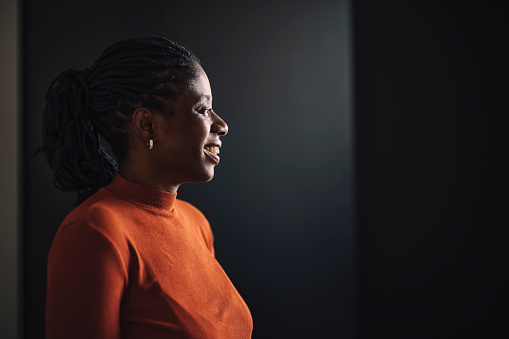 Happy businesswoman in orange shirt standing over a black background and looking away